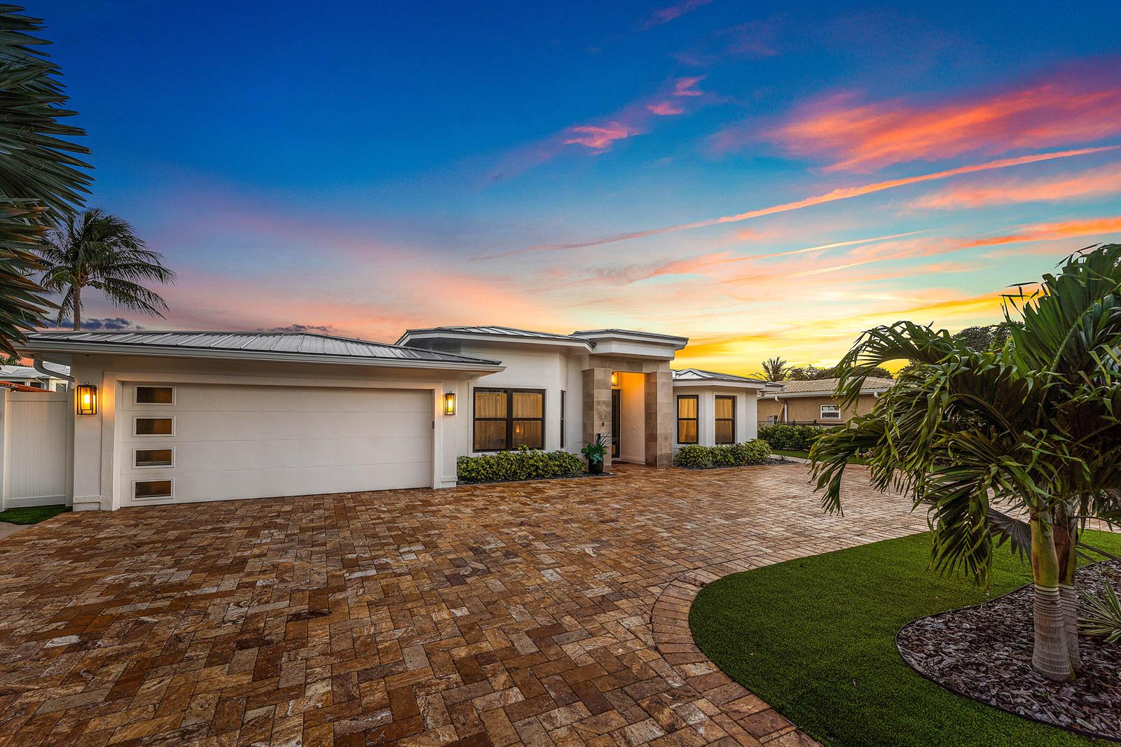 A modern single-story house with a white exterior, paver driveway, and palm trees at sunset — 680 NE Harbour Drive, Boca Raton FL 33431, BOCA RATON, FL