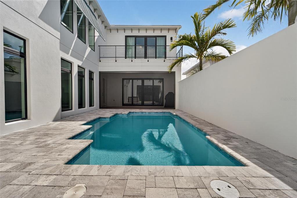 A rectangular swimming pool sits in a paved courtyard between two white exterior walls — 5917 CAT CLAW LANE, BRADENTON, FL