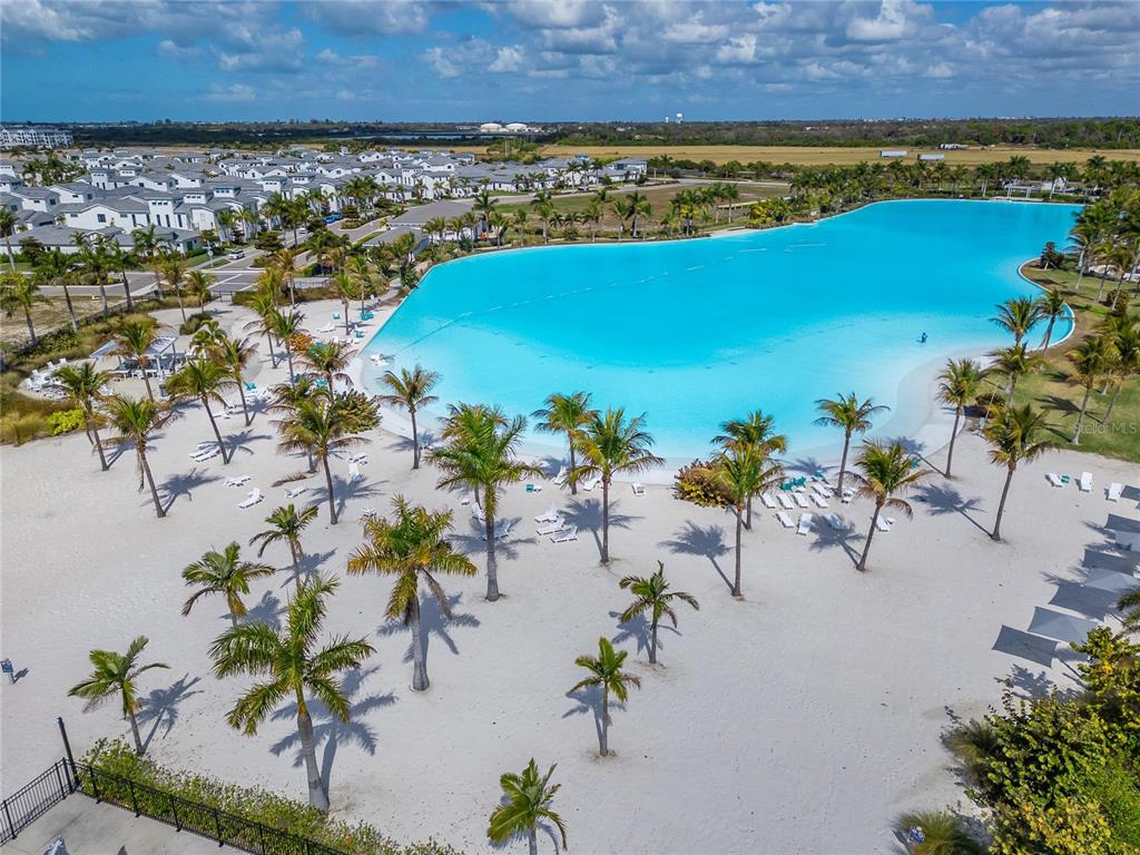 An aerial view shows a large turquoise lagoon surrounded by a sandy beach and palm trees — 5917 CAT CLAW LANE, BRADENTON, FL