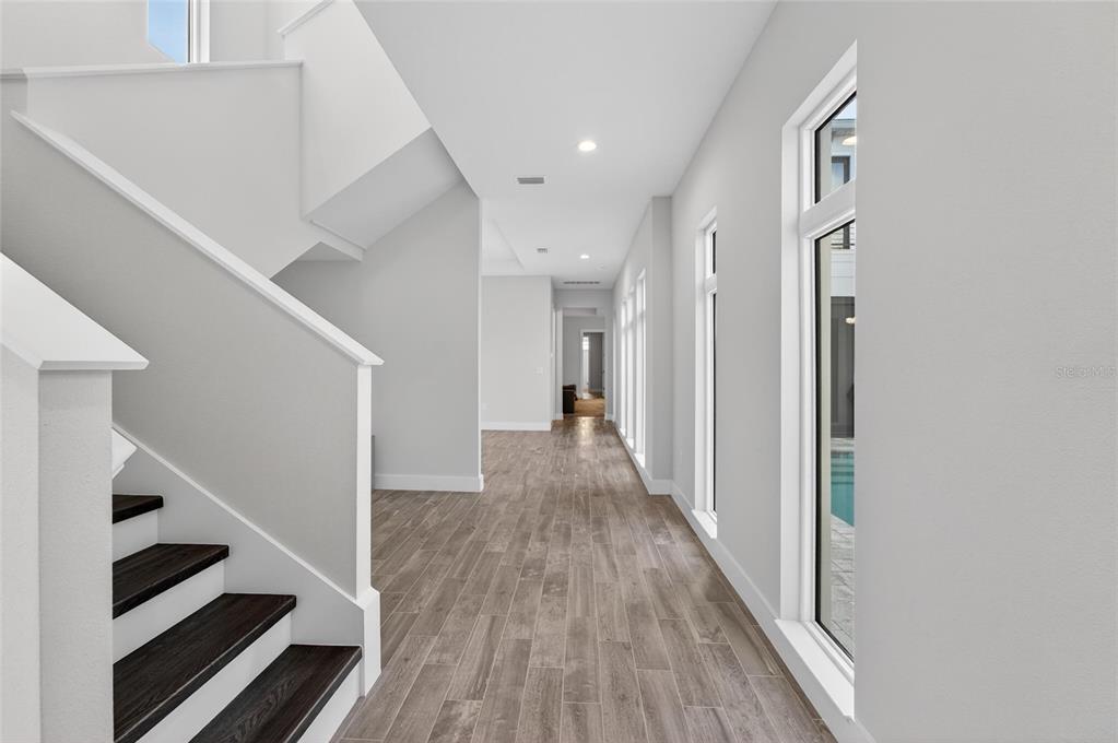 A bright hallway features wood-look tile flooring, a staircase with dark treads, and tall windows — 5917 CAT CLAW LANE, BRADENTON, FL