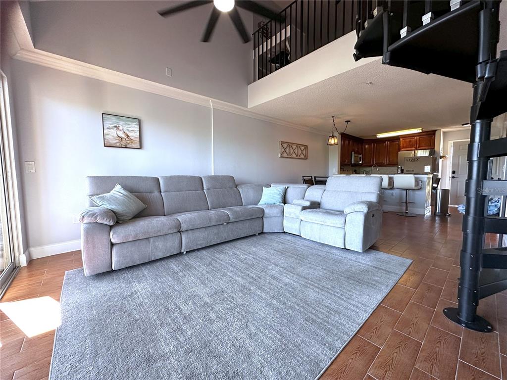A living room with a grey sectional sofa, area rug, and a black spiral staircase — 2400 FEATHER SOUND DRIVE UNIT 534, CLEARWATER, FL
