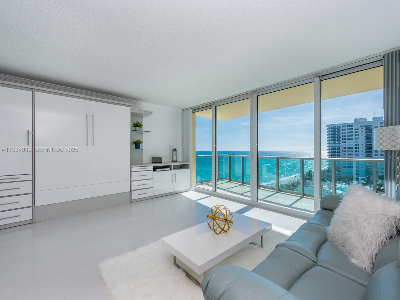 A modern living room features a white wall unit, a light blue sofa, and ocean views — 2501 S Ocean Dr, Hollywood FL 33019, HOLLYWOOD, FL
