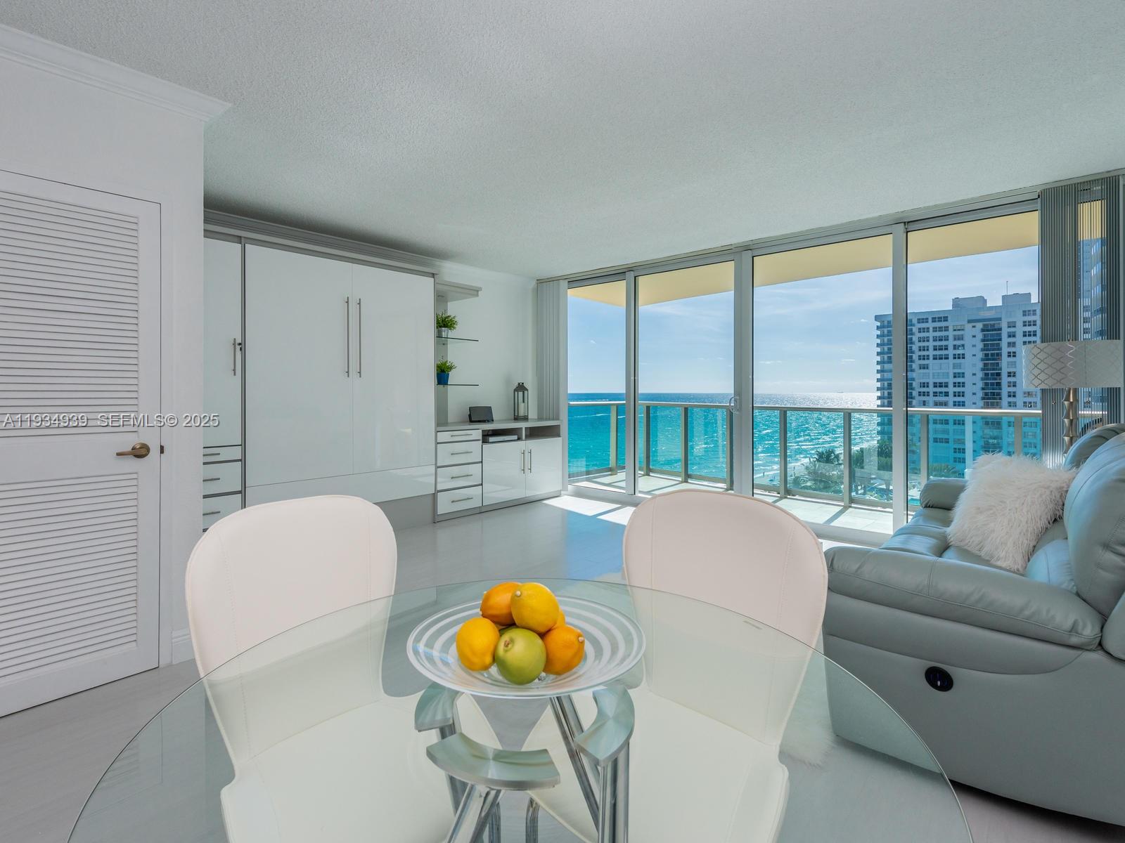 A dining area with a glass table overlooks the ocean through floor-to-ceiling sliding glass doors — 2501 S Ocean Dr, Hollywood FL 33019, HOLLYWOOD, FL