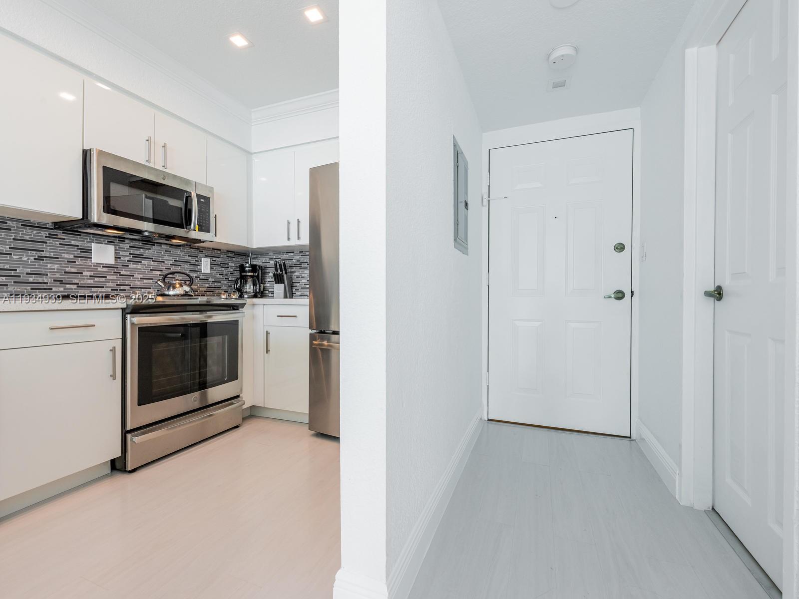 A kitchen with white cabinets and stainless steel appliances sits beside a white entryway door — 2501 S Ocean Dr, Hollywood FL 33019, HOLLYWOOD, FL