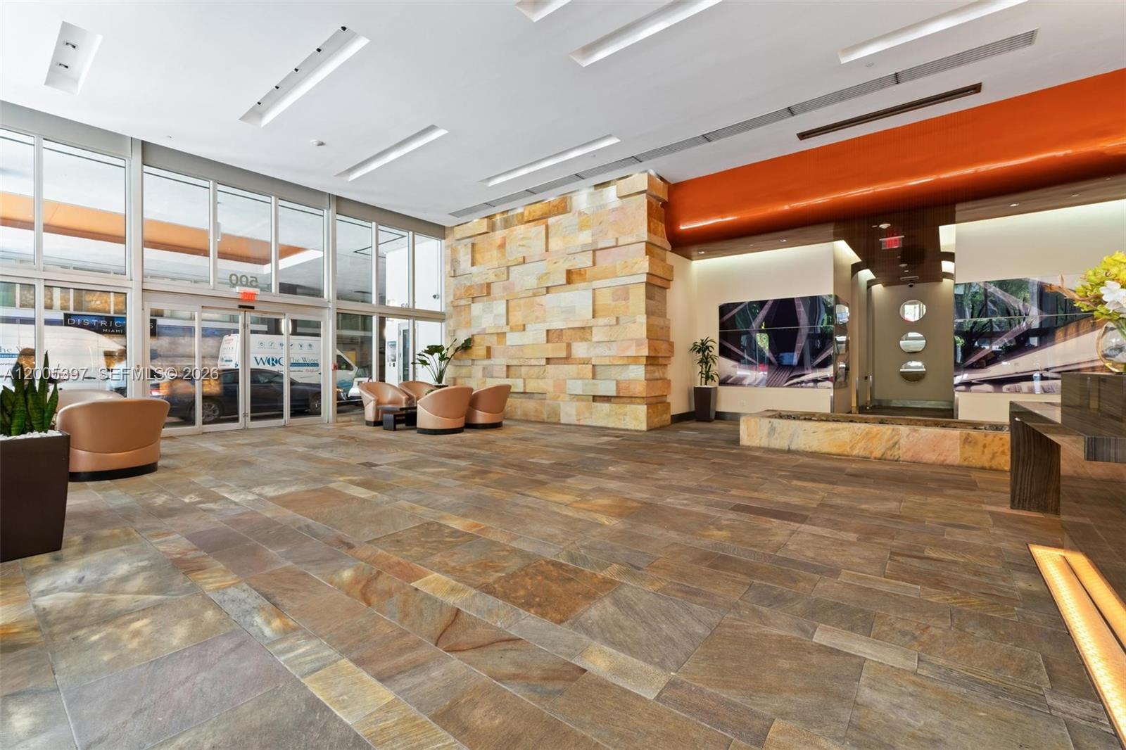 A modern building lobby features stone tile flooring, a textured stone accent wall, and seating — 500 Brickell Ave # 1405, Miami FL 33131, MIAMI, FL