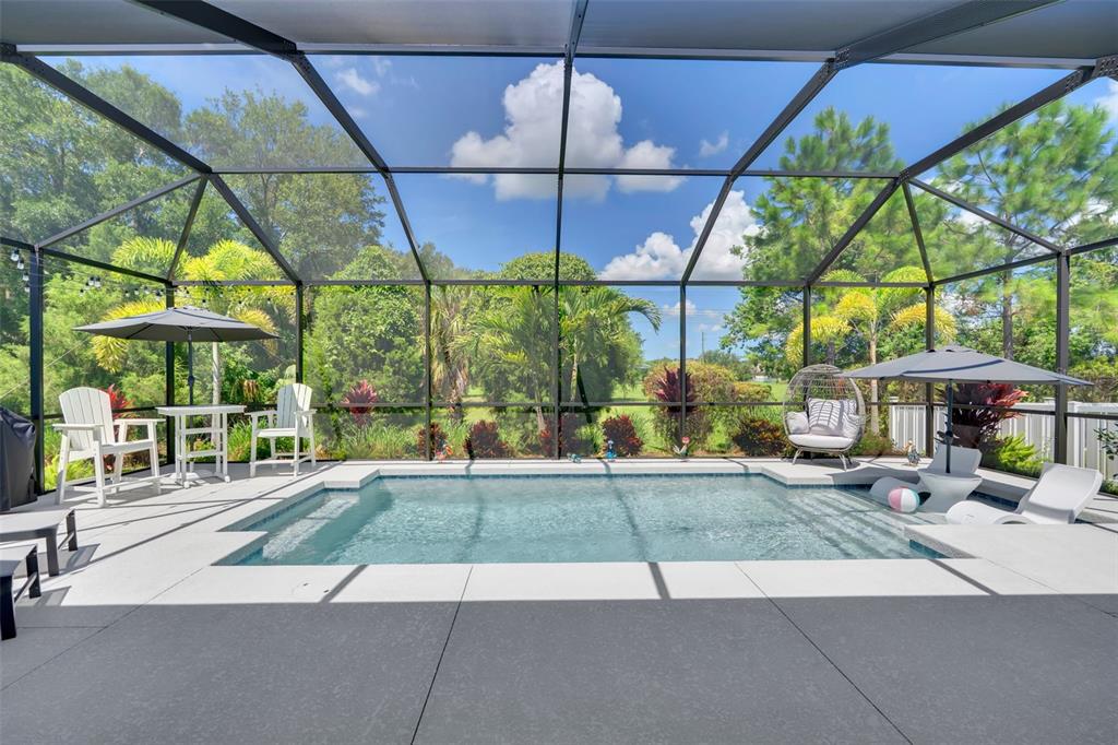 A swimming pool with a screened enclosure, patio furniture, and umbrellas in a backyard setting — 3321 WOODMONT DRIVE, PARRISH, FL