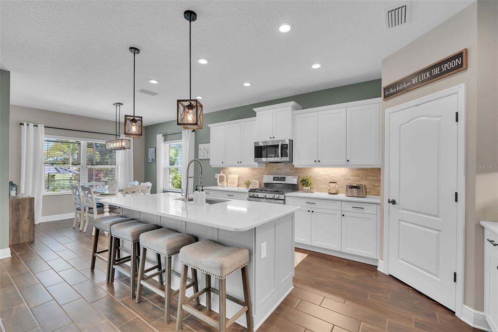 A modern kitchen features a white island with bar stools, white cabinetry, and wood-look tile flooring — 3321 WOODMONT DRIVE, PARRISH, FL
