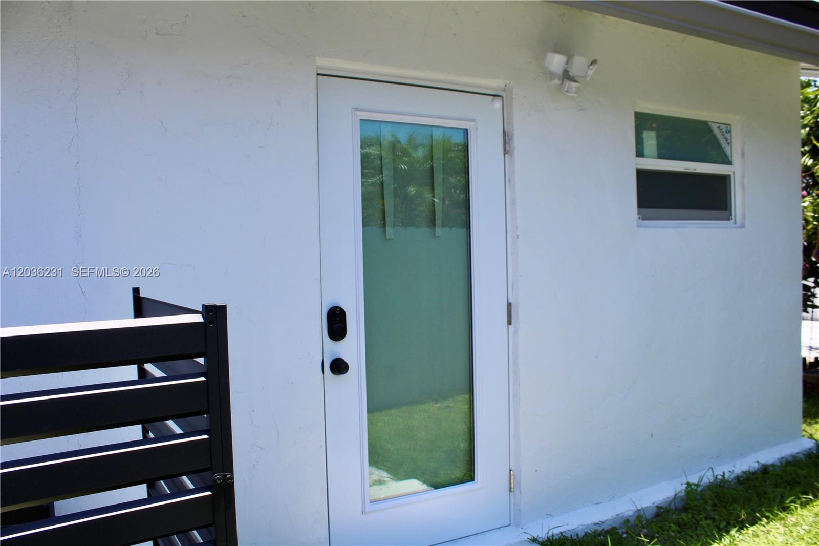 A white exterior wall features a glass-paneled door, a small window, and a black fence — 14670 SW 150th St # A, Miami FL 33186, MIAMI, FL