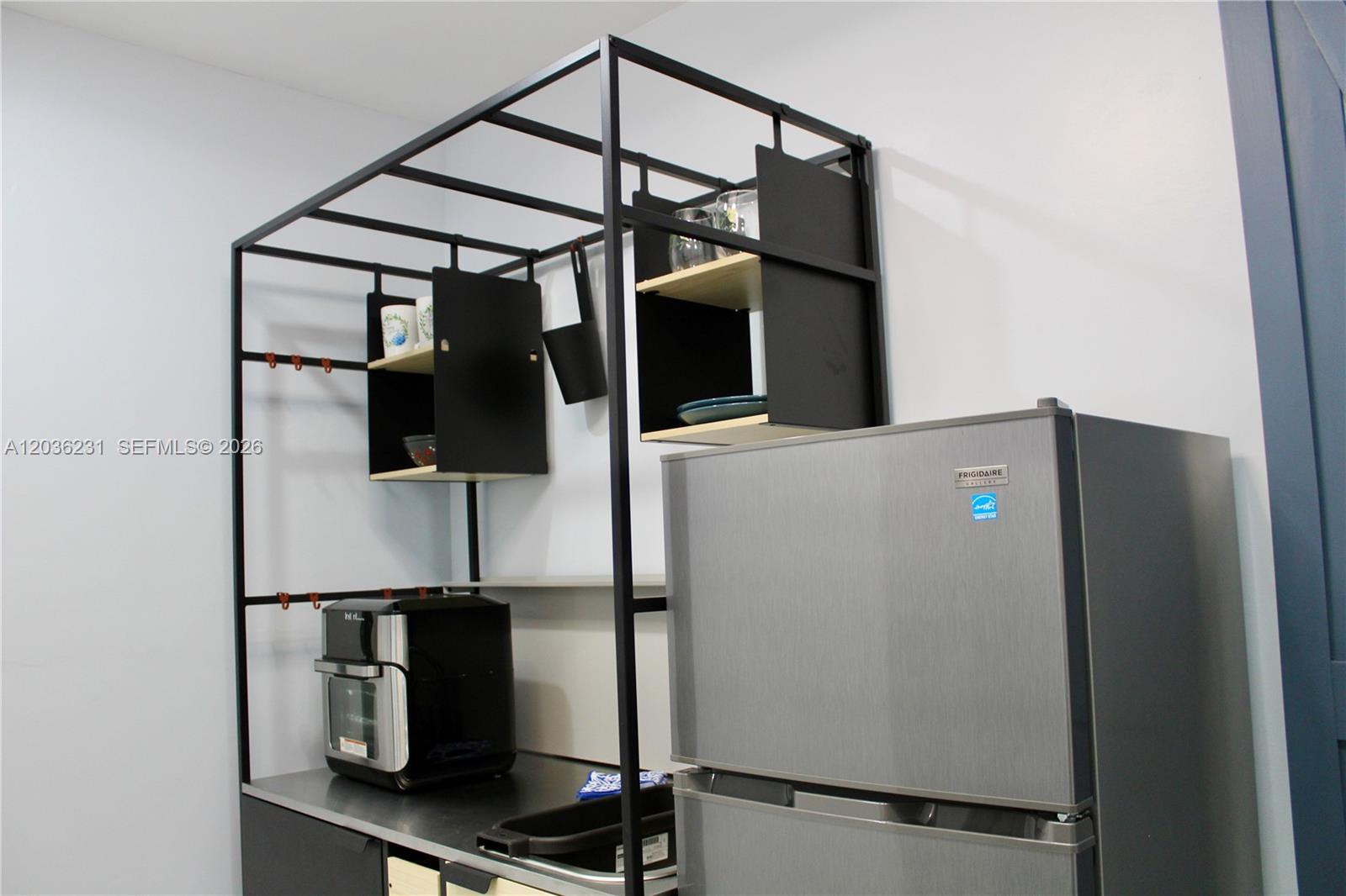 A kitchen area features a black metal shelving unit, stainless steel countertop, and a refrigerator — 14670 SW 150th St # A, Miami FL 33186, MIAMI, FL