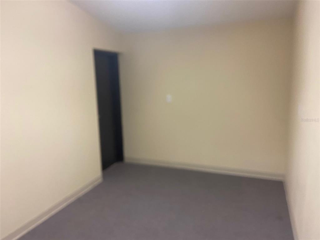 An empty room with beige walls, gray carpeting, and a single dark door — 3434 SW 24TH AVENUE UNIT B, GAINESVILLE, FL