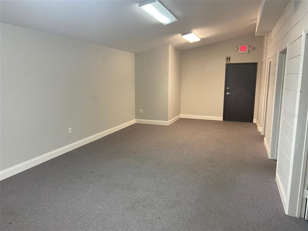 An empty room with gray carpet, light gray walls, two ceiling lights, and a dark door — 3434 SW 24TH AVENUE UNIT B, GAINESVILLE, FL