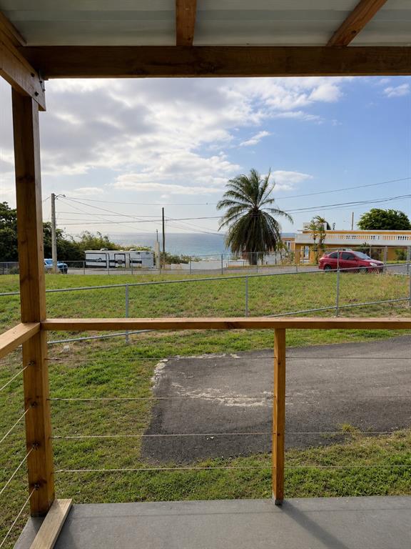A view of a grassy yard and the ocean from a wooden porch with railings — CALLE PASCUA URB. MANUEL CORCHADO, ISABELA, PR