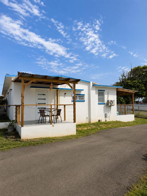 A white one-story house with a wooden porch, metal roof, and an asphalt driveway — CALLE PASCUA URB. MANUEL CORCHADO, ISABELA, PR