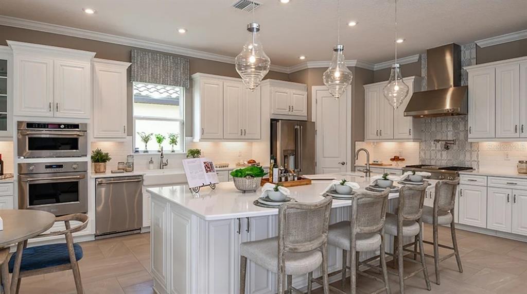 A bright kitchen features white cabinetry, a large central island, and stainless steel appliances — 29680 IMPERATI BOULEVARD, WESLEY CHAPEL, FL