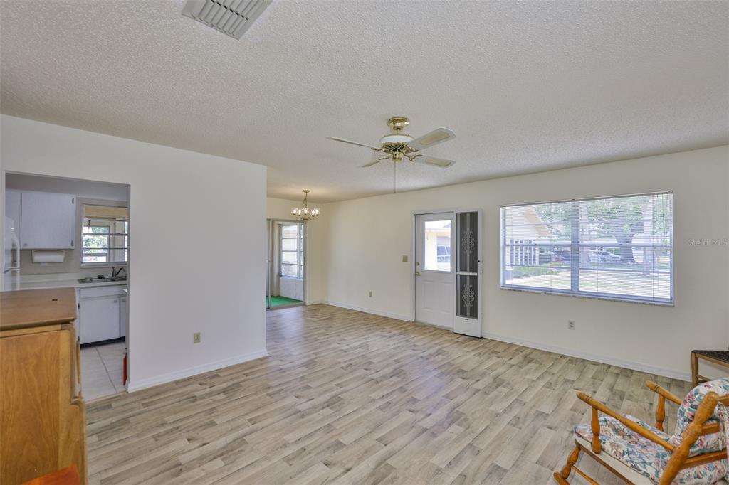 A living room with wood-look flooring, a ceiling fan, and a view into the kitchen — 1904 CANTERBURY LANE UNIT 18, SUN CITY CENTER, FL