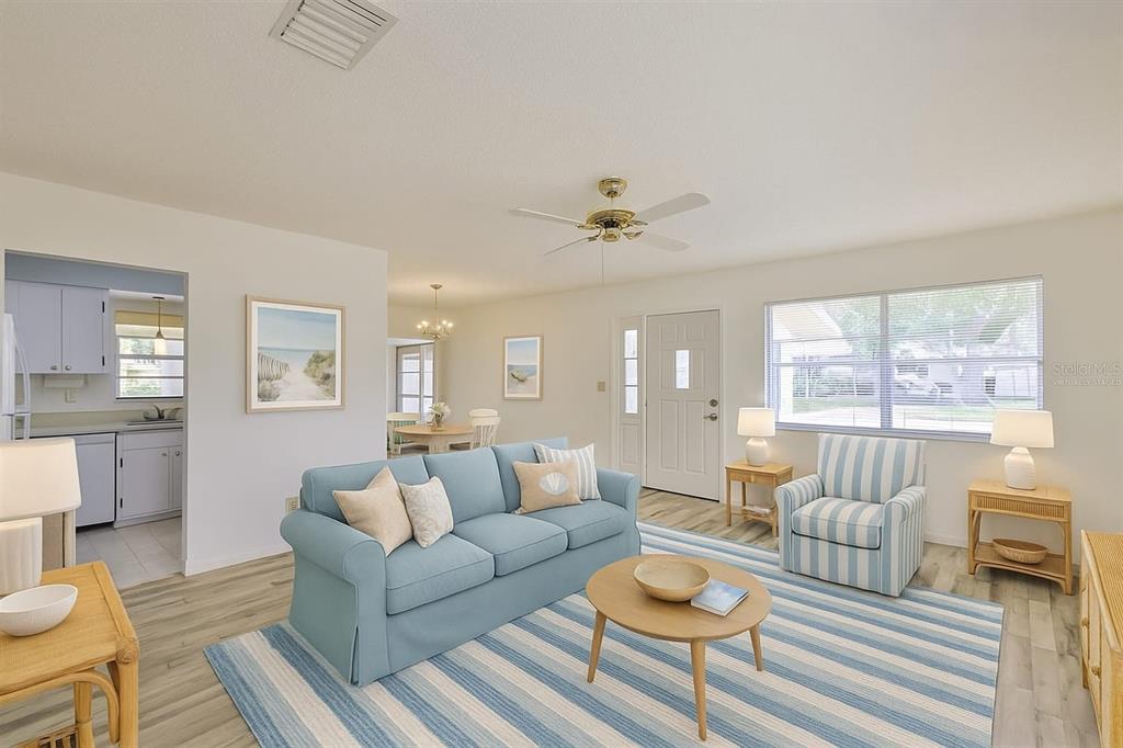 A living room with light wood floors, a blue sofa, striped armchair, and area rug — 1904 CANTERBURY LANE UNIT 18, SUN CITY CENTER, FL