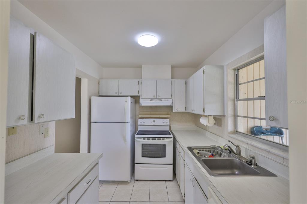A kitchen features white cabinets, white appliances, a stainless steel sink, and tiled flooring — 1904 CANTERBURY LANE UNIT 18, SUN CITY CENTER, FL