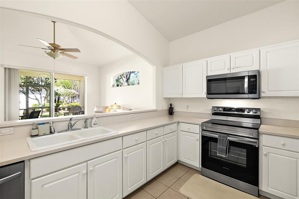 A kitchen with white cabinets, stainless steel appliances, and a pass-through window to a living area — 17 ARBOR TRACE UNIT 17, PALM COAST, FL
