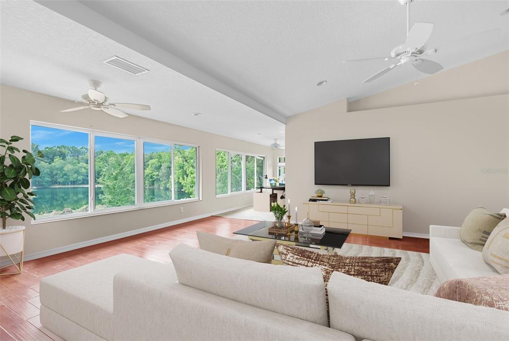 A living room features a large sectional sofa, a wall-mounted television, and floor-to-ceiling lake views — 9986 E NEW HOPE COURT, FLORAL CITY, FL