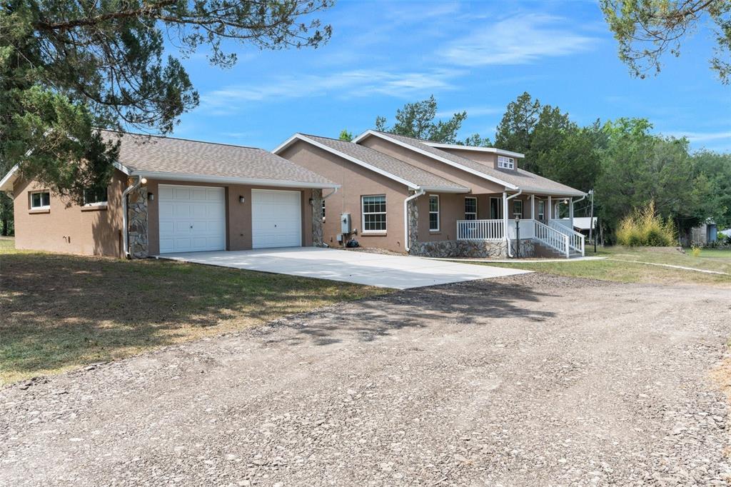 A tan house with a stone foundation, attached two-car garage, and a front porch — 9986 E NEW HOPE COURT, FLORAL CITY, FL