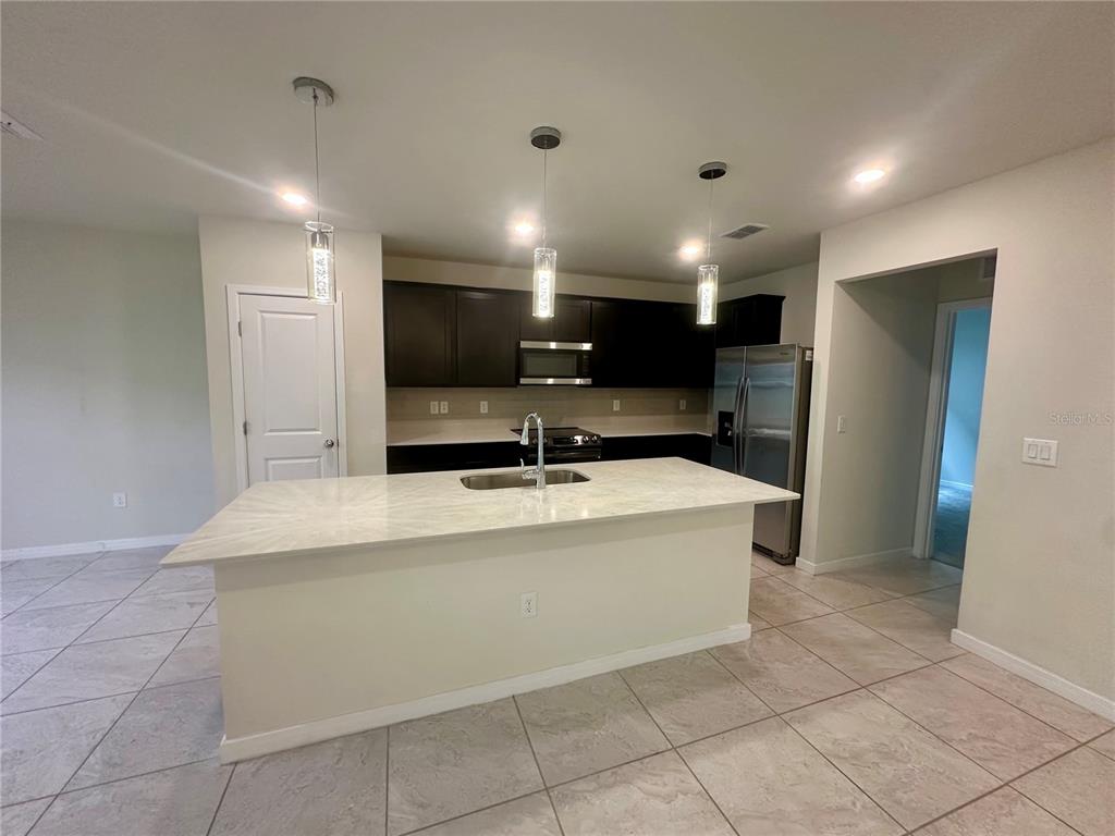 A kitchen features dark cabinets, a white quartz island with a sink, and tile flooring — 1261 REGAL KING DRIVE, KISSIMMEE, FL