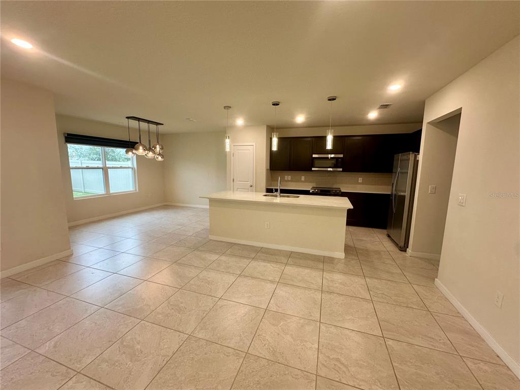 A kitchen with dark cabinets, a central island, and tile flooring opens to a dining area — 1261 REGAL KING DRIVE, KISSIMMEE, FL