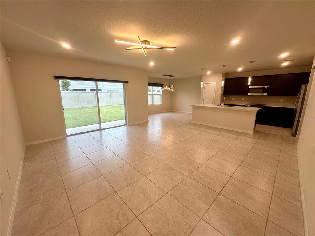 An open-concept kitchen and living area features light tile flooring and a sliding glass door — 1261 REGAL KING DRIVE, KISSIMMEE, FL