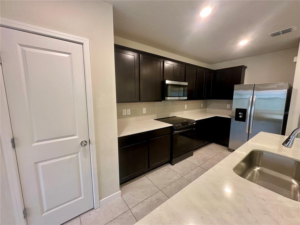 A kitchen features dark wood cabinets, stainless steel appliances, and white countertops with tile flooring — 1261 REGAL KING DRIVE, KISSIMMEE, FL