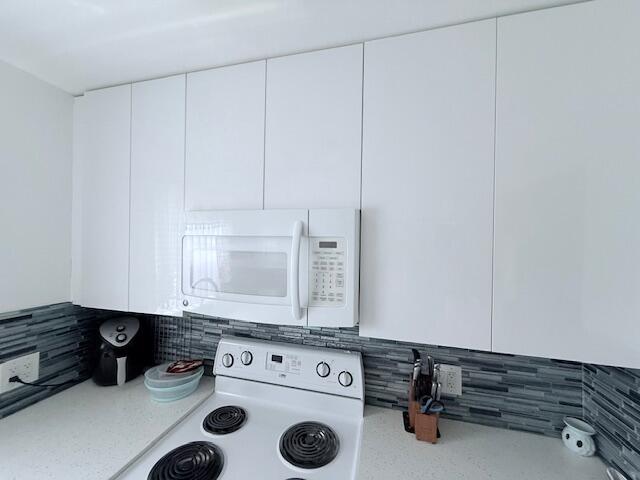 A kitchen features white flat-panel cabinets, a white microwave, and a gray tiled backsplash — 41 Upminster B Crescent # B, Deerfield Beach FL 33442, DEERFIELD BEACH, FL