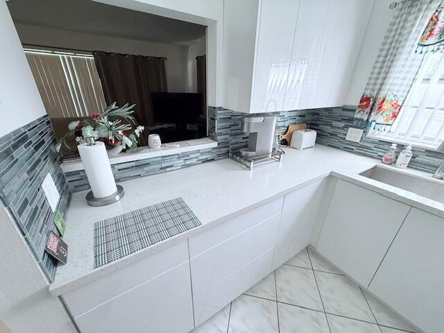 A modern kitchen features white cabinets, quartz countertops, and a blue glass tile backsplash — 41 Upminster B Crescent # B, Deerfield Beach FL 33442, DEERFIELD BEACH, FL