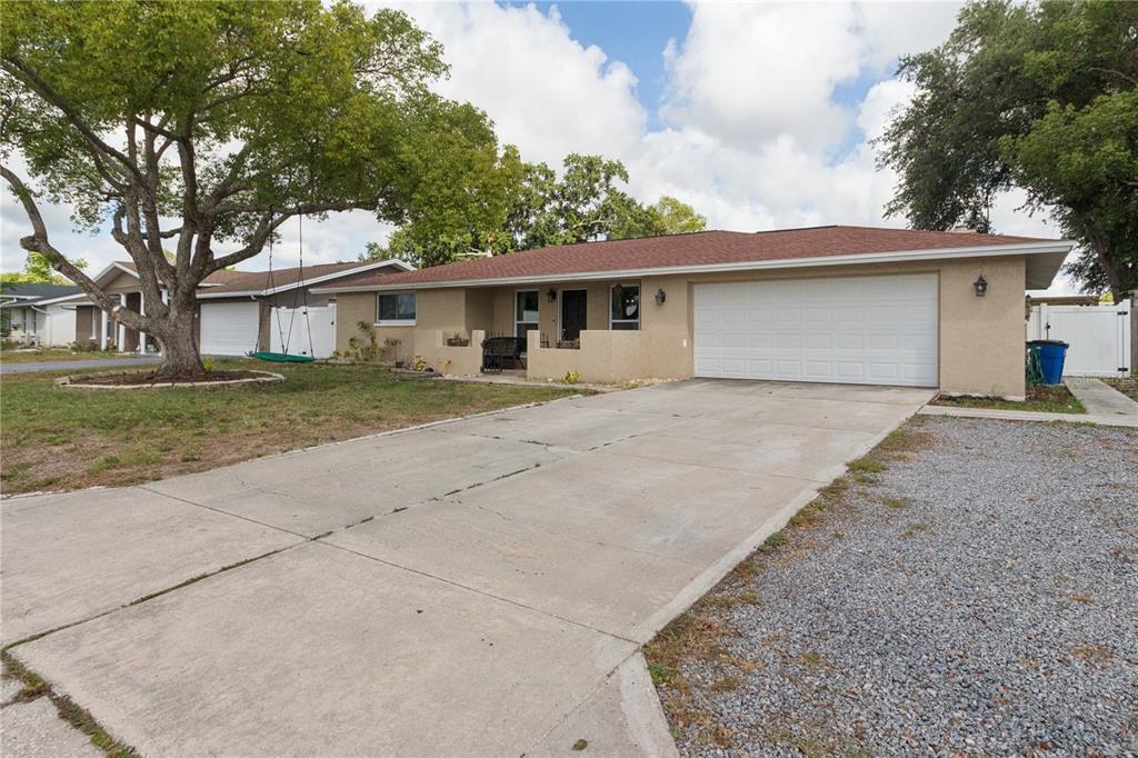 A single-story house with a tan stucco exterior, a red roof, and a concrete driveway — 7528 SCOTTIE DRIVE, PORT RICHEY, FL