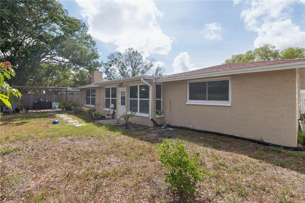 The exterior of a tan, single-story house features a backyard with a patio and trees — 7528 SCOTTIE DRIVE, PORT RICHEY, FL