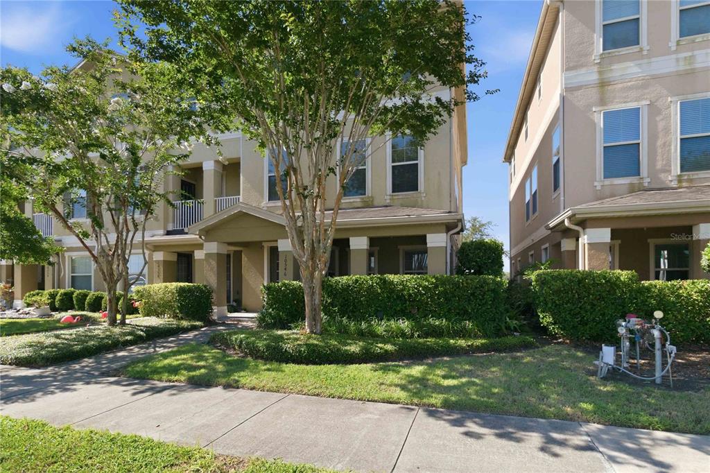 A three-story townhouse exterior features a covered front porch, tan stucco siding, and landscaping — 10546 GREEN IVY LANE, ORLANDO, FL