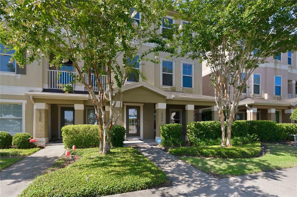 A two-story townhouse exterior features a covered entryway, tan stucco walls, and mature trees — 10546 GREEN IVY LANE, ORLANDO, FL