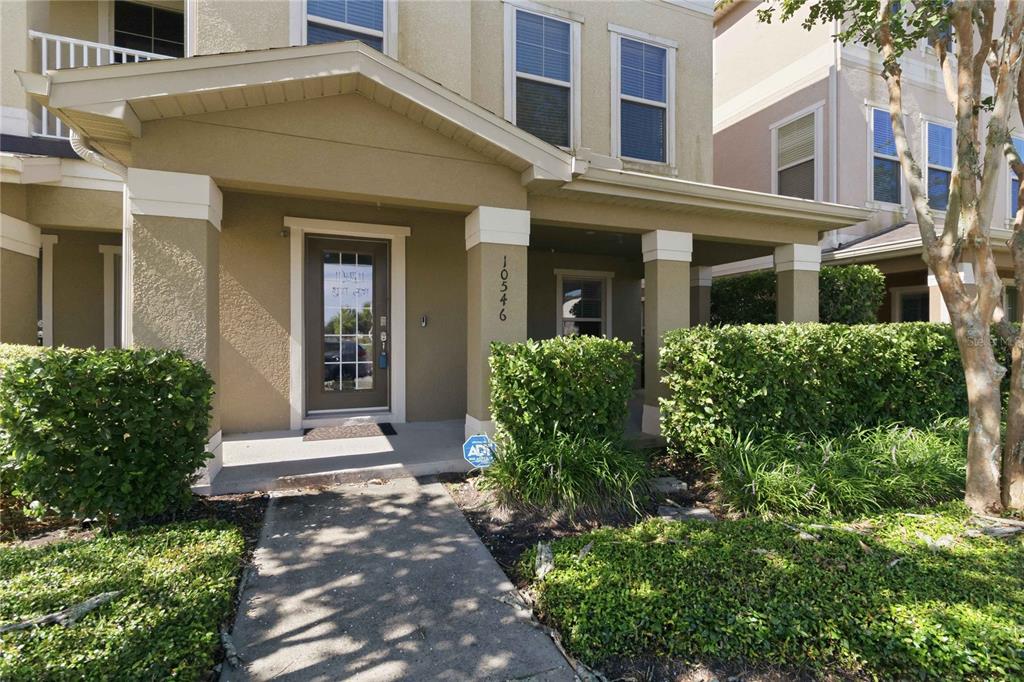 The exterior of a two-story tan house features a covered front porch and walkway — 10546 GREEN IVY LANE, ORLANDO, FL