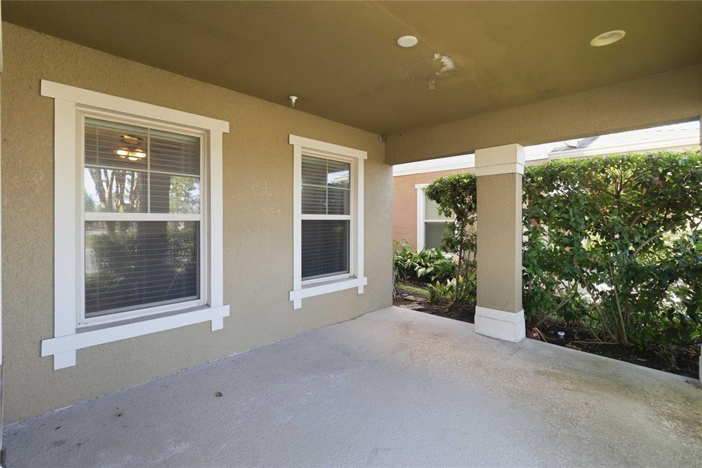 A covered concrete patio features two windows with white trim and a support column — 10546 GREEN IVY LANE, ORLANDO, FL