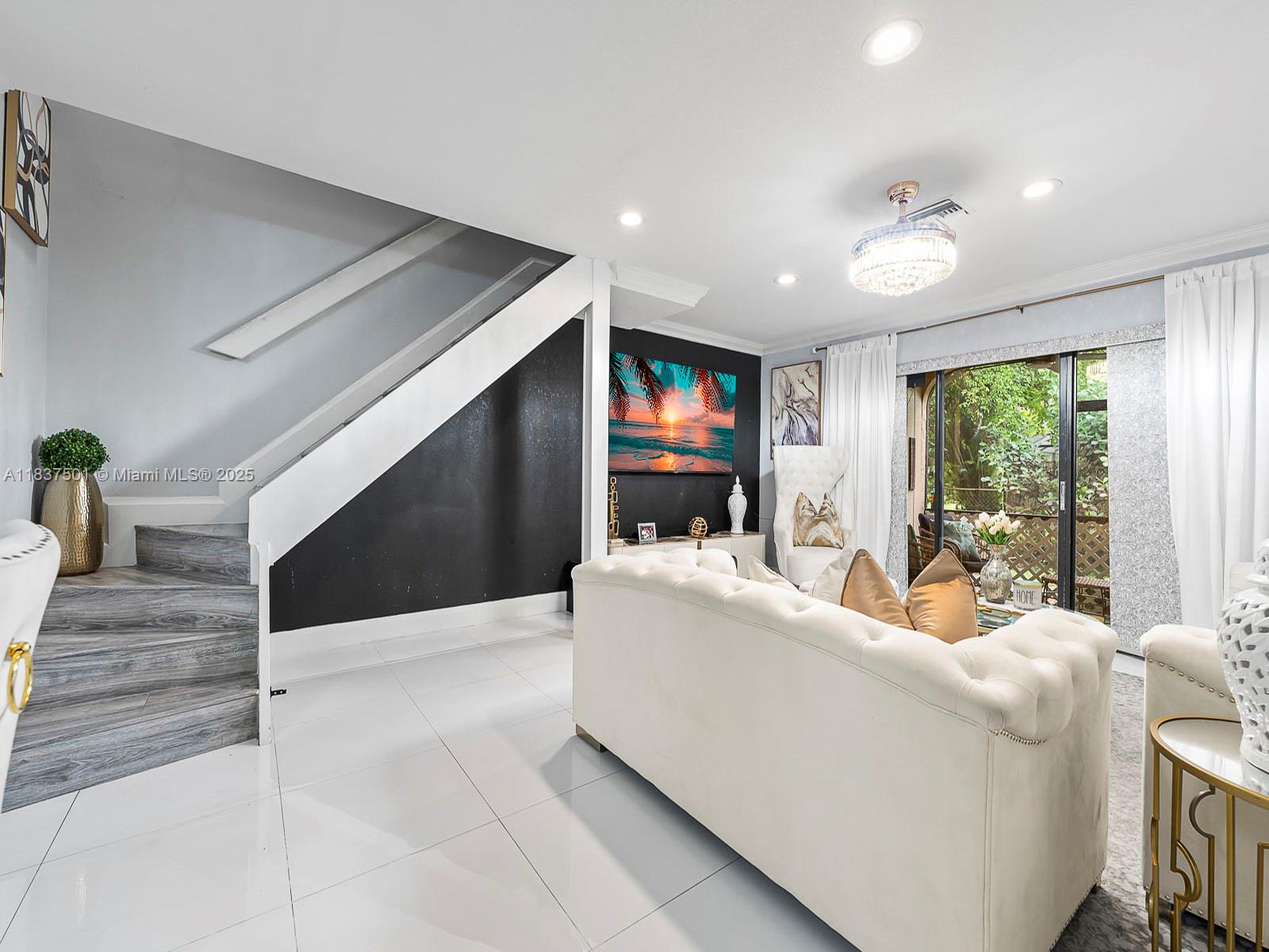 A living room features a white tufted sofa, a staircase, and a wall-mounted television — 10942 W Sample Rd # E1, Coral Springs FL 33065, CORAL SPRINGS, FL