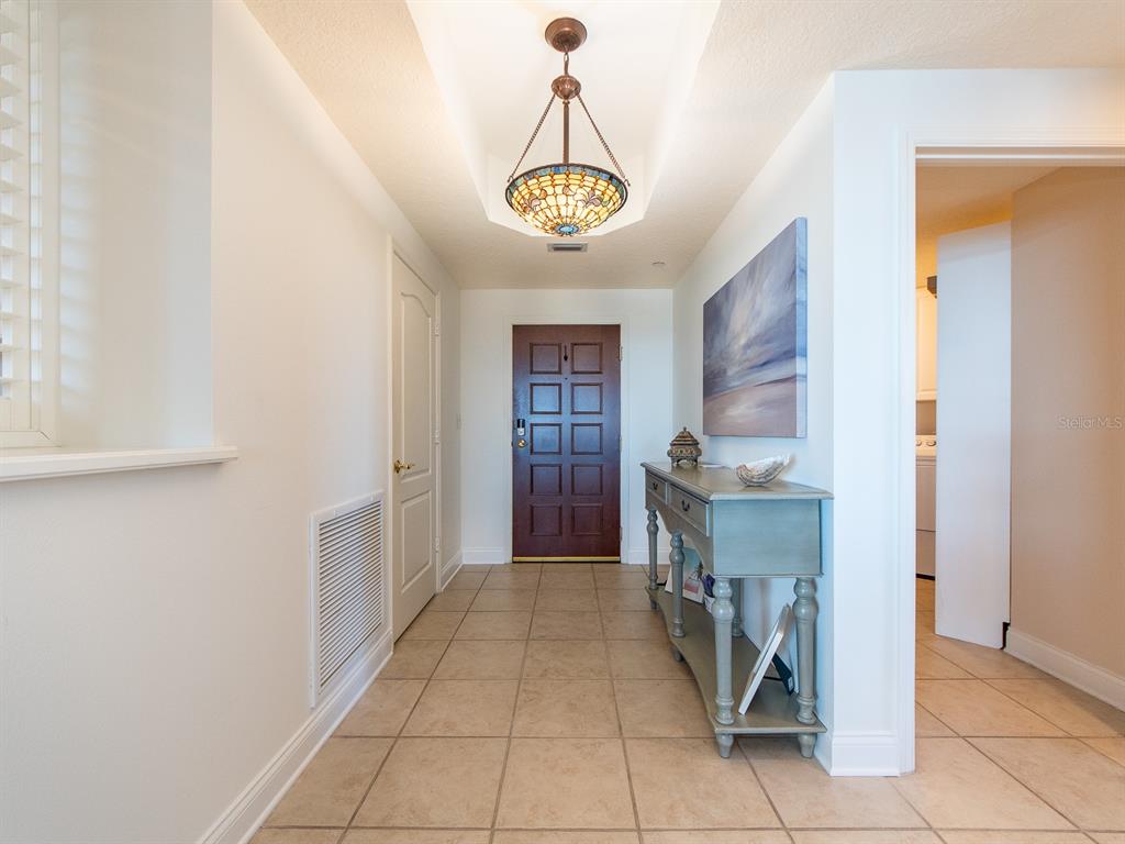 A tiled entryway features a dark wood front door, a console table, and a pendant light — 521 MANDALAY AVENUE UNIT 410, CLEARWATER BEACH, FL