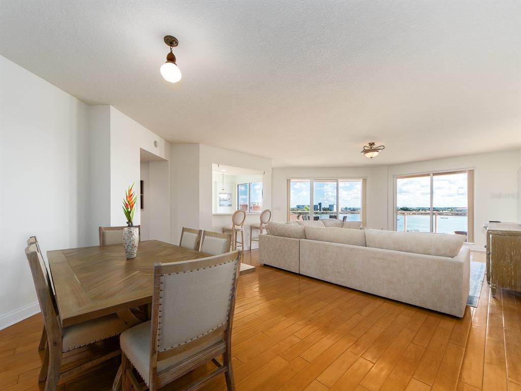 A dining area with a wooden table leads into a living room with water views — 521 MANDALAY AVENUE UNIT 410, CLEARWATER BEACH, FL