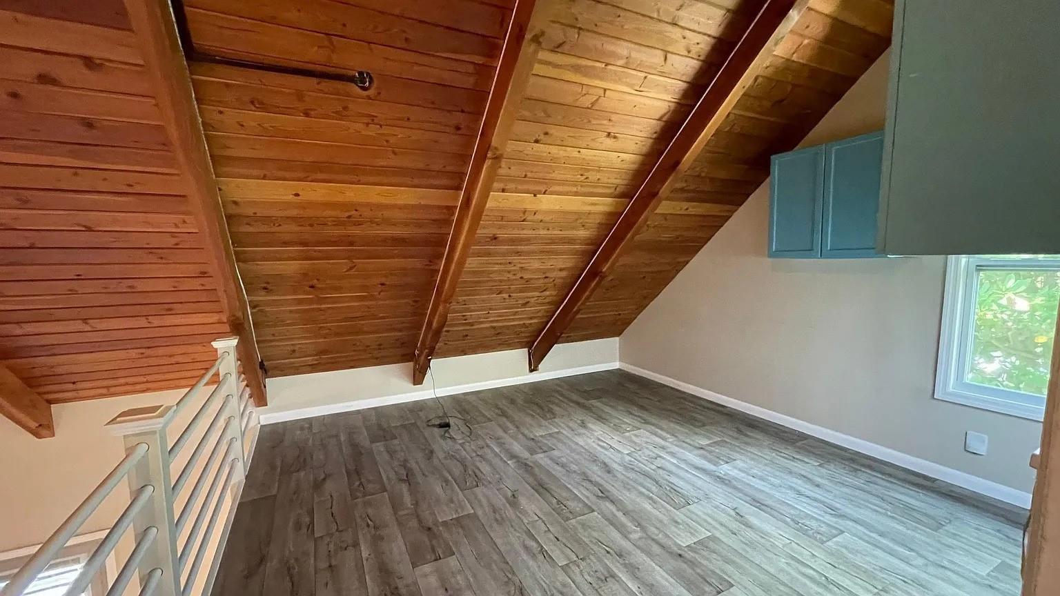 An attic room features wood-paneled vaulted ceilings, gray wood-look flooring, and a metal stair railing — 24 Bonita Avenue, Key Largo FL, KEY LARGO, FL