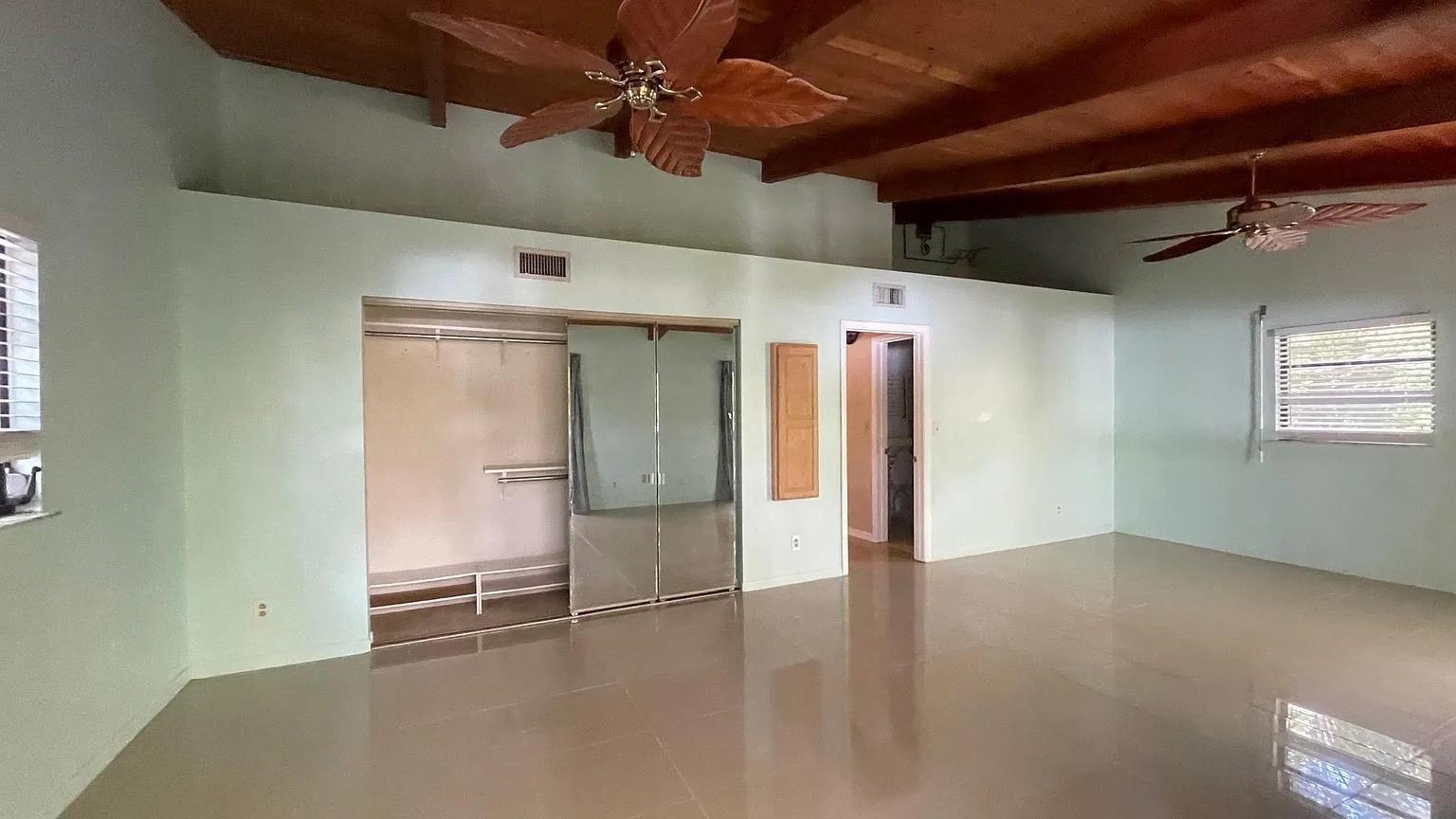 A bedroom with light green walls, tiled floors, mirrored closet doors, and wood-beamed ceilings — 24 Bonita Avenue, Key Largo FL, KEY LARGO, FL