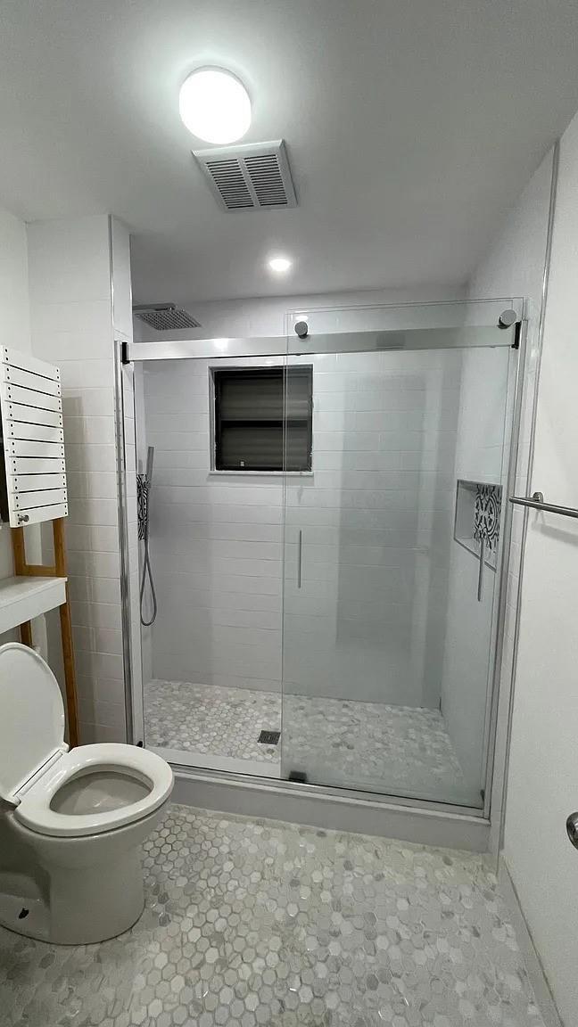 A bathroom featuring a glass-enclosed shower with pebble flooring, white subway tiles, and a toilet — 24 Bonita Avenue, Key Largo FL, KEY LARGO, FL
