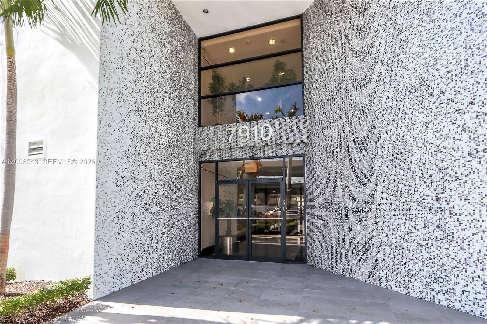 The entrance to a building features a glass door and a mosaic-tiled facade — 7910 NW 25th St # 207, Doral FL 33122, DORAL, FL