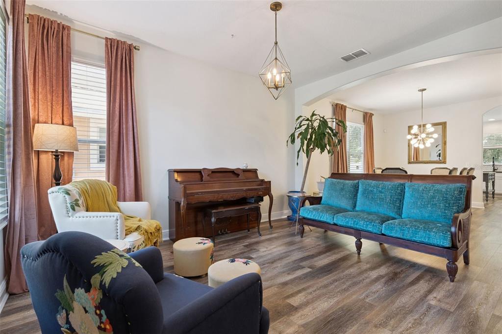 A living room features a piano, a teal sofa, two armchairs, and wood-look flooring — 509 SPRING RIVER DRIVE, ORLANDO, FL