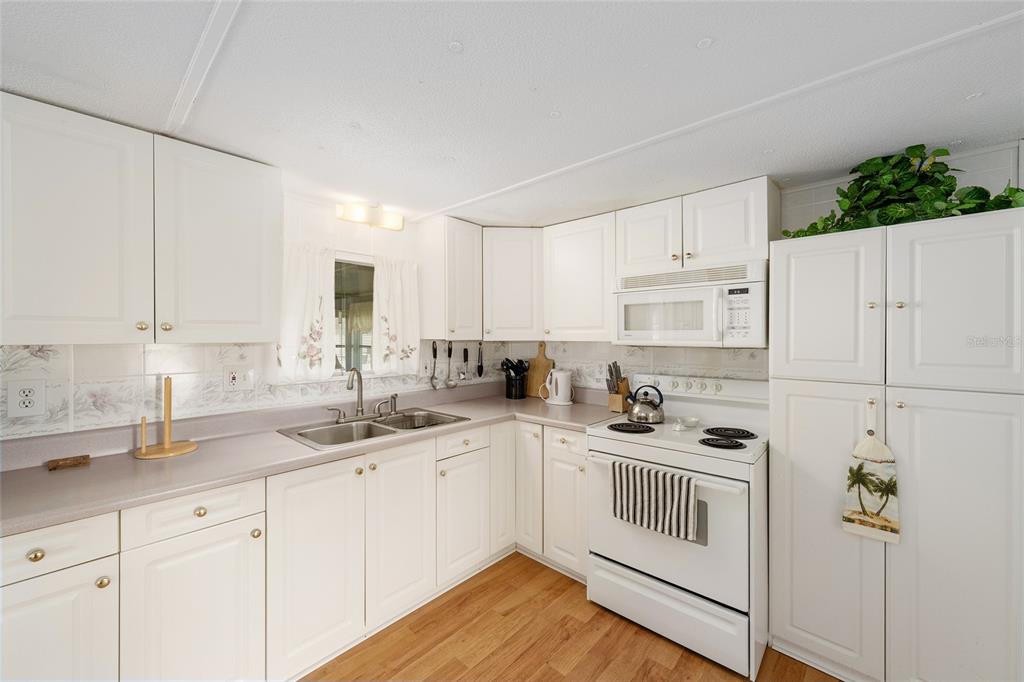 A kitchen with white cabinets, laminate countertops, a white stove, and wood-look flooring — 1027 VERMONT AVENUE, LADY LAKE, FL