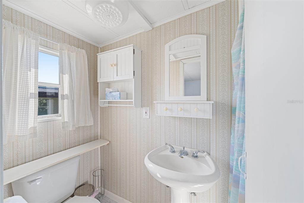 A bathroom features a pedestal sink, a toilet, a wall-mounted cabinet, and striped wallpaper — 1027 VERMONT AVENUE, LADY LAKE, FL