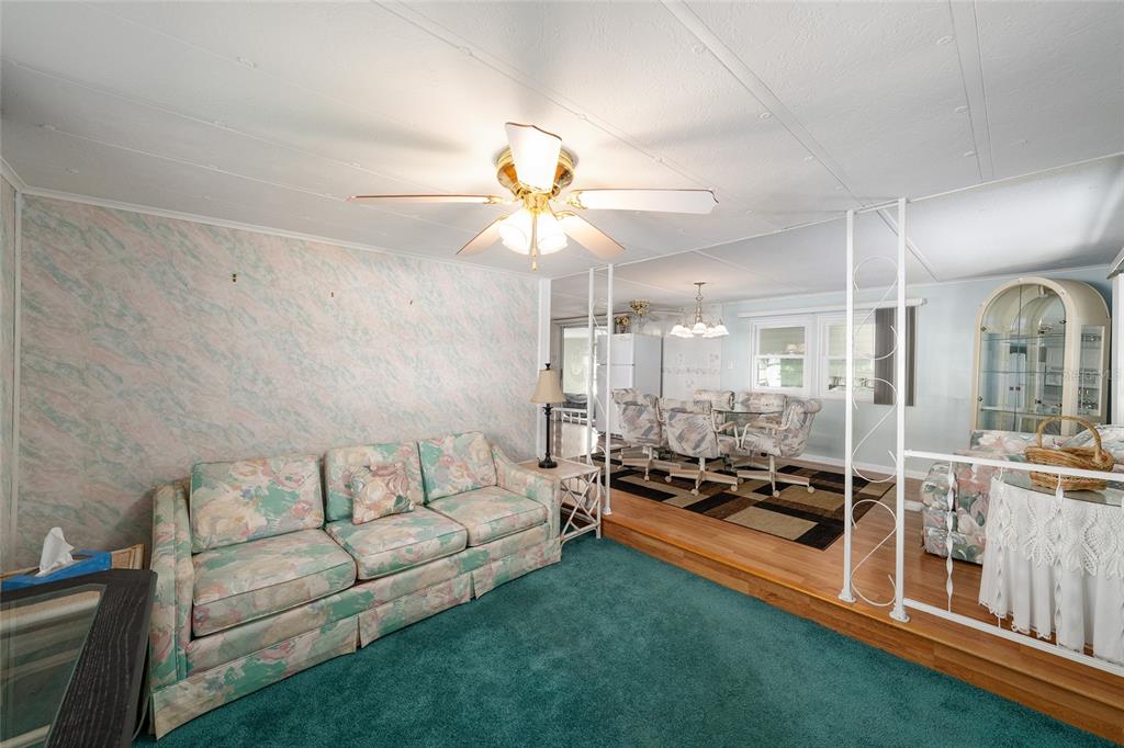 A living room with teal carpeting and floral furniture sits beside a raised dining area — 1027 VERMONT AVENUE, LADY LAKE, FL
