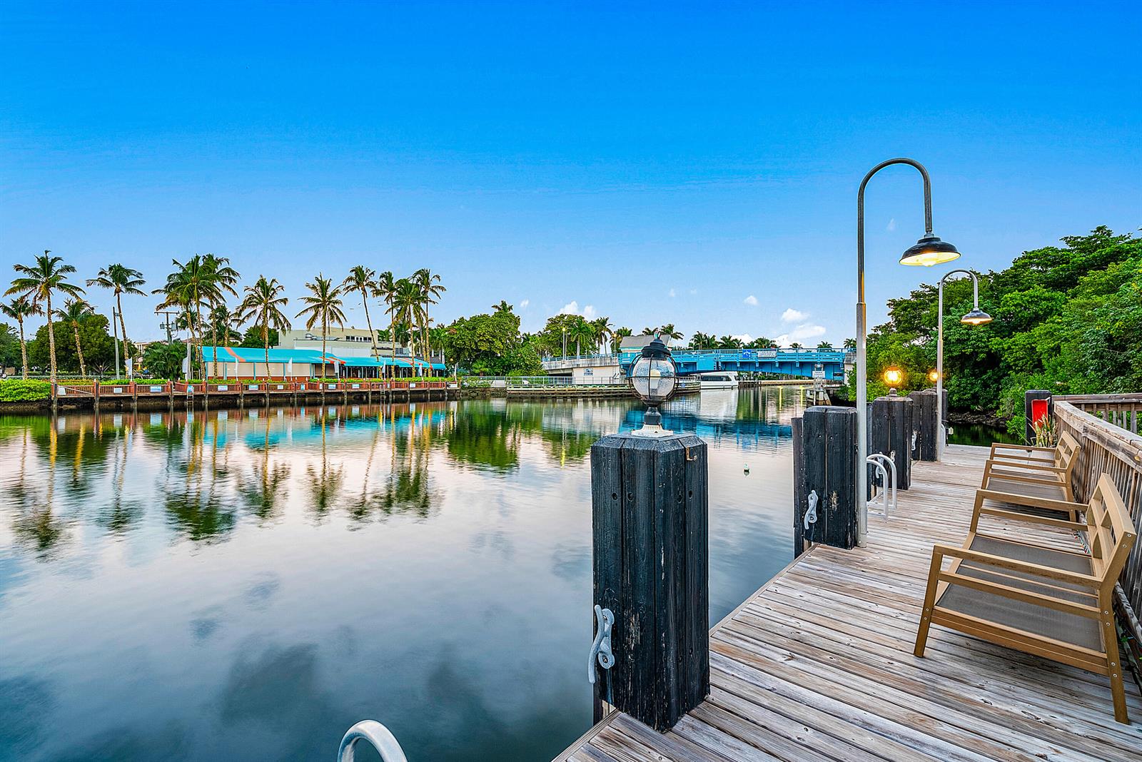 A wooden dock with seating overlooks a calm canal with palm trees and a blue bridge — 900 E Atlantic Avenue # 22, Delray Beach FL 33483, DELRAY BEACH, FL
