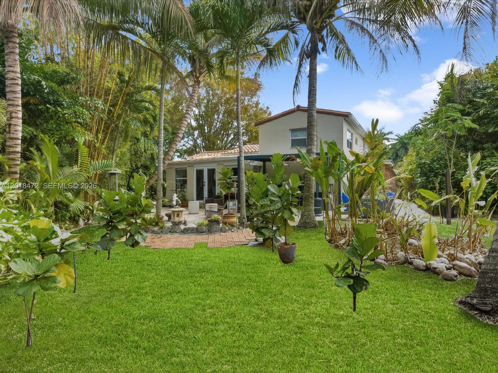 A backyard features a green lawn, potted plants, palm trees, and a two-story house — 357 NE 117th St, Miami FL 33161, MIAMI, FL