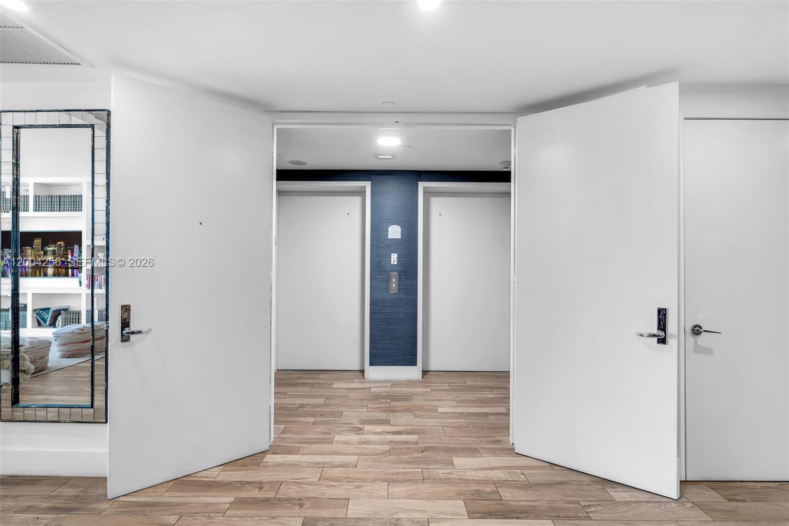 A hallway with wood-look flooring leads to two elevator doors set against a blue wall — 791 Crandon Blvd # 302, Key Biscayne FL 33149, KEY BISCAYNE, FL